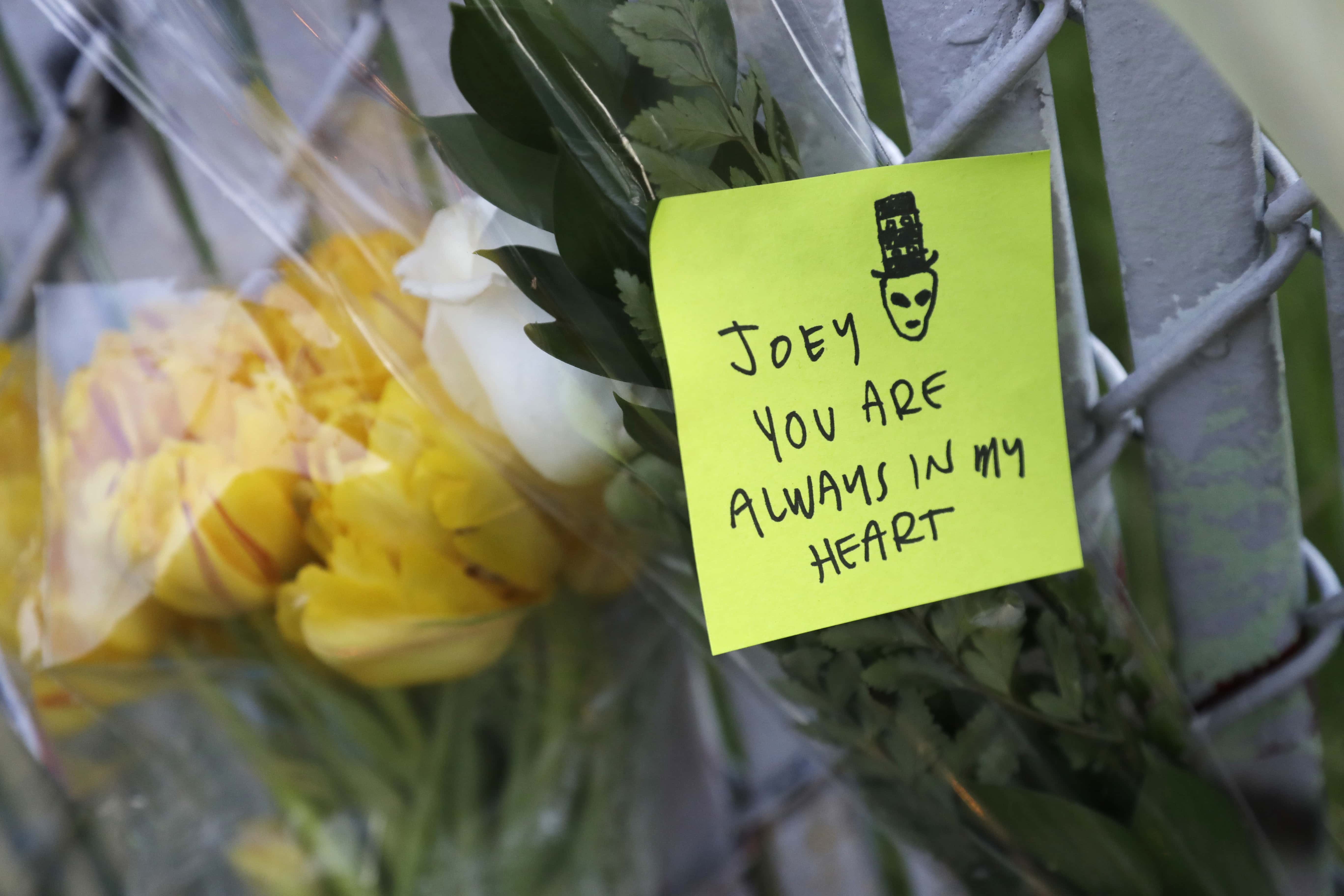 A note with flowers hangs on a fence near the site of a warehouse fire Monday, Dec. 5, 2016, in Oakland, Calif. The death toll in the Oakland warehouse on Friday fire climbed Monday with more bodies still feared buried in the blackened ruins, and families anxiously awaited word of their missing loved ones. (AP Photo/Marcio Jose Sanchez)