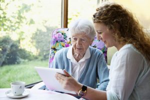 Nurse assisting elderly woman in reading from a tablet computer, an example of patient-centered care.