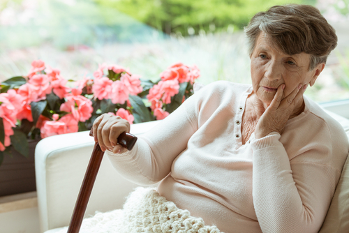 Elderly woman sitting in thought with a blanket on during early winter.