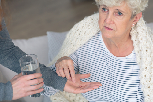 Elderly woman taking her medication witha  blanket on during winter.