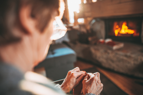 Elderly woman sewing in front of a fire place during winter.