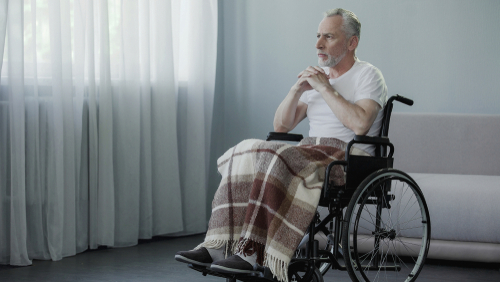 Elderly man in a wheelchair sitting inside in the dark, which can exacerbate Seasonal Affective Disorder.