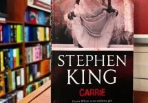 Paperback cover of Carrie by Stephen King shown on a bookshop shelf background