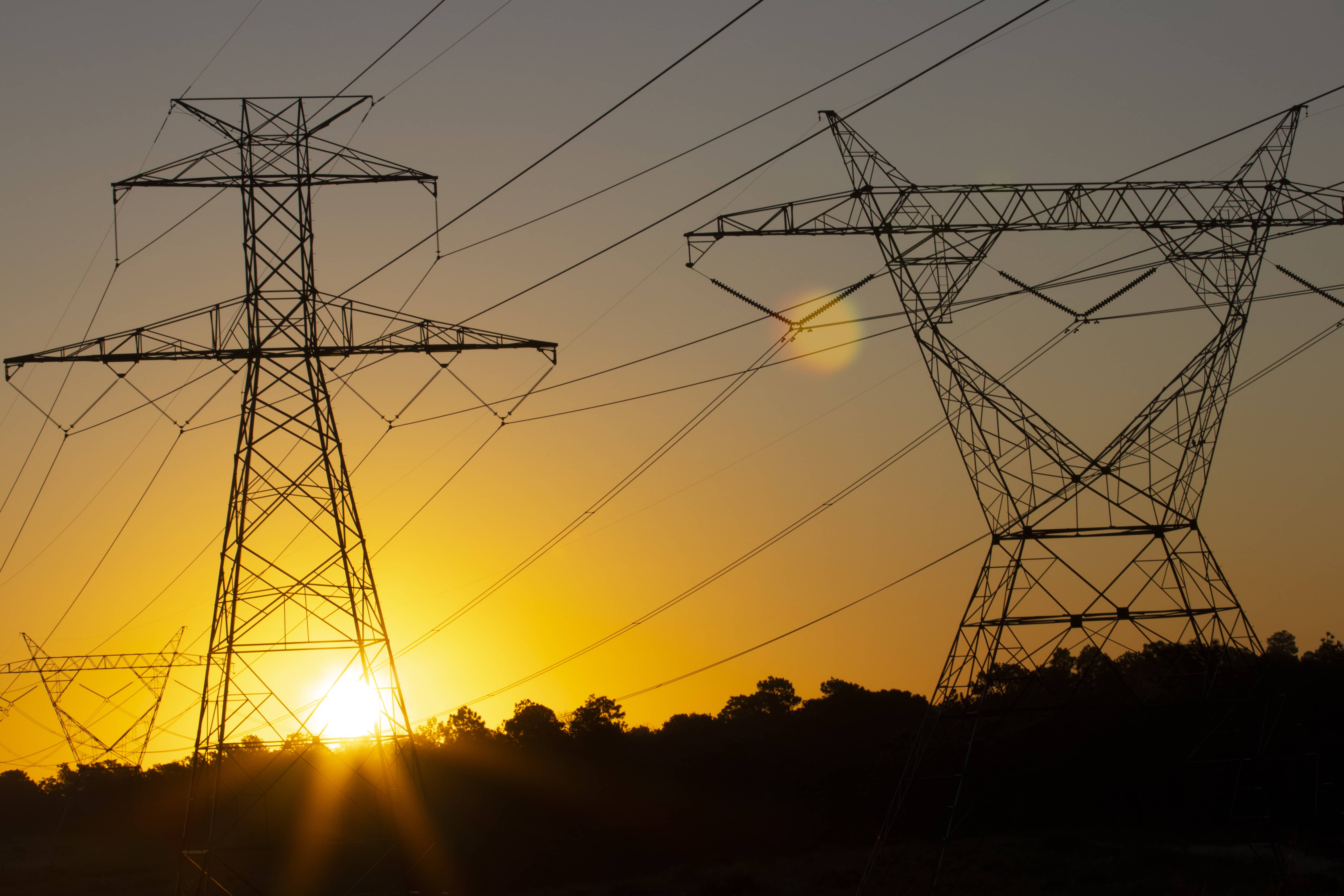 the-sun-rising-behind-a-pair-of-towering-electricity-pylons