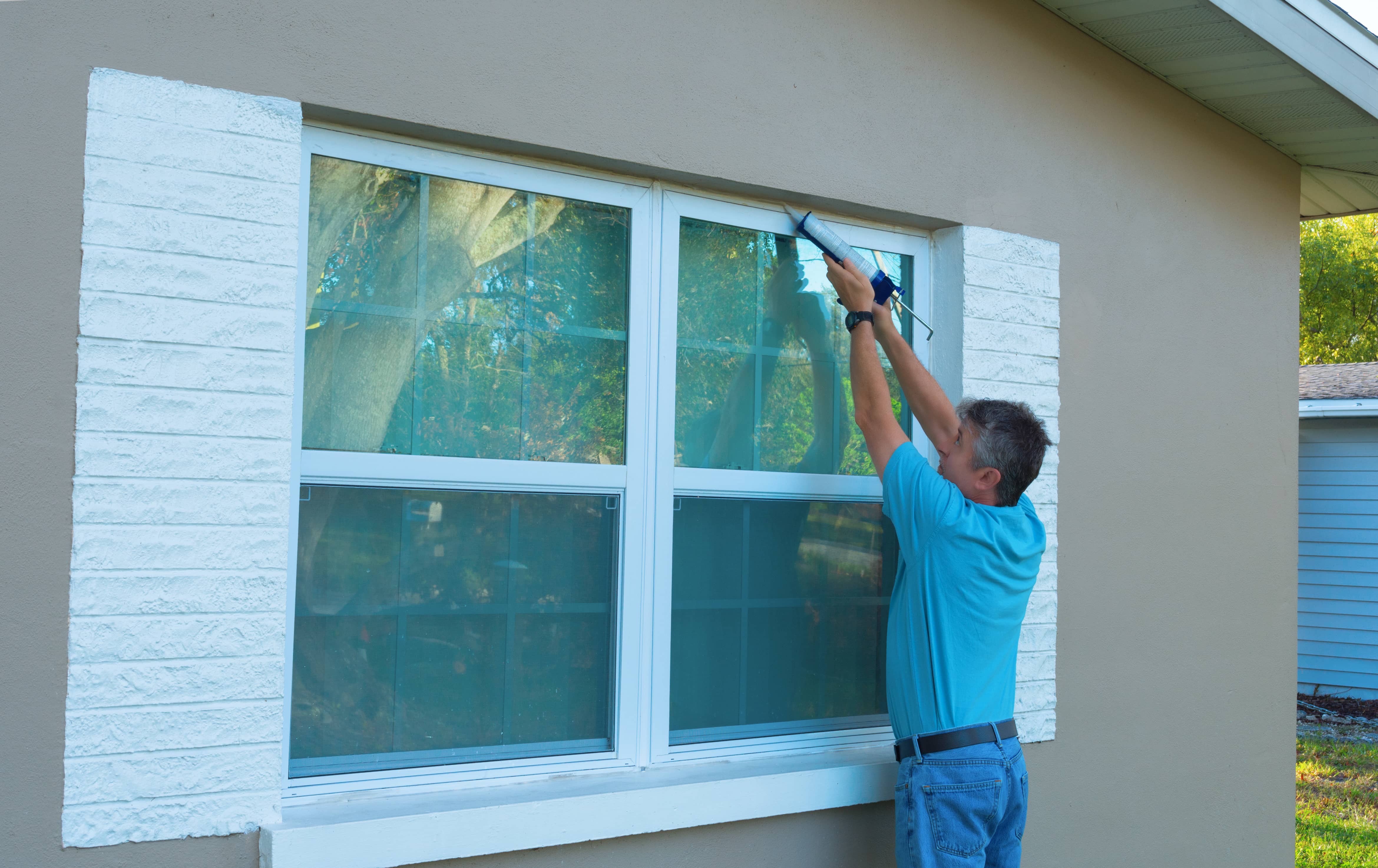 homeowner-caulking-window-with-a-caulk-gun-an-important-part-of-weatherproofing-homes-and-houses-against-rain-wind-hurricanes-and-storms