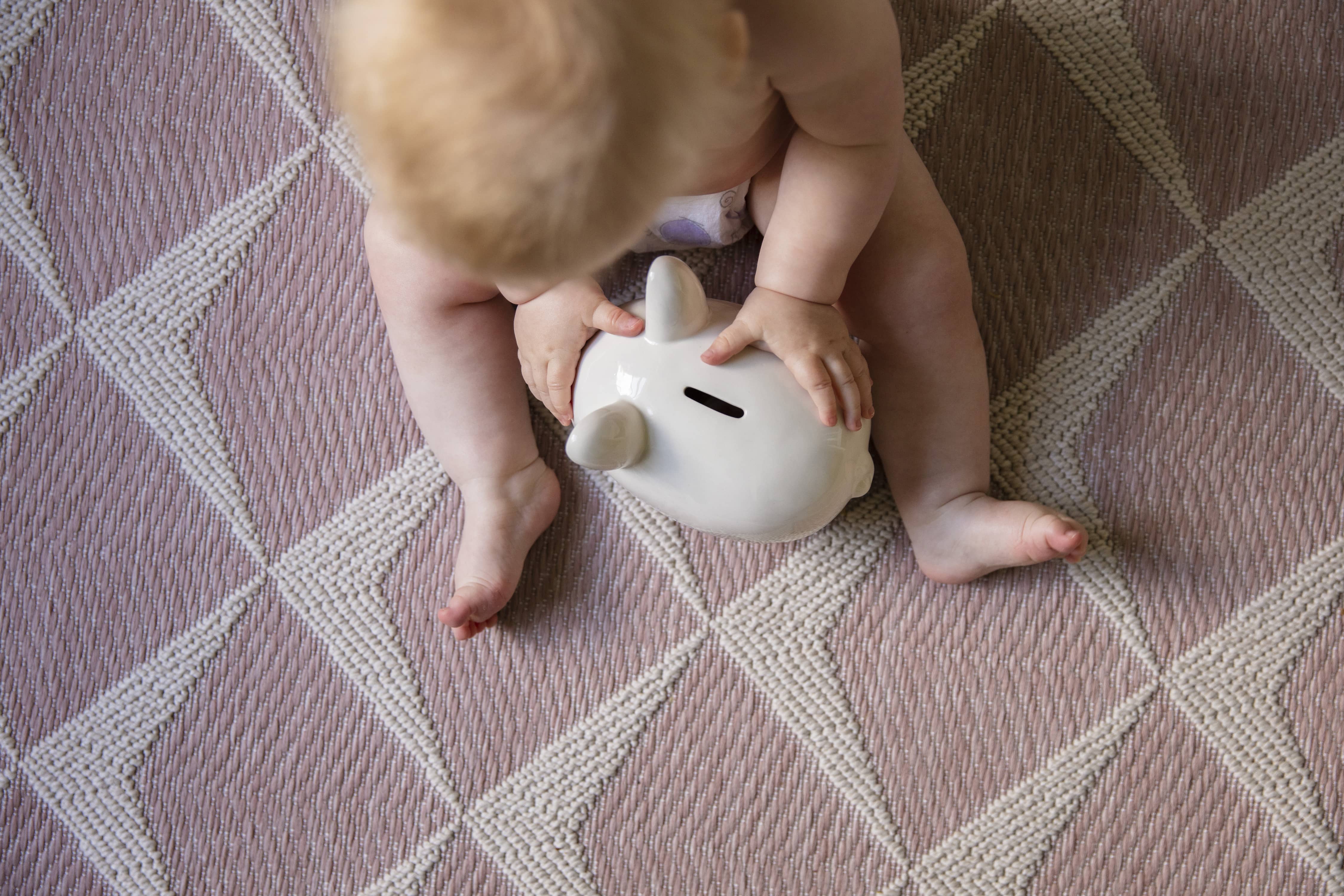 baby-starts-saving-early-overhead-view-of-baby-playing-with-a-piggy-bank