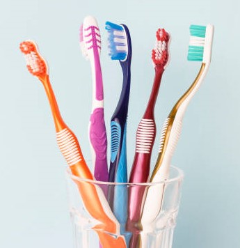 multi-colored-toothbrushes-in-a-glass-cup-blue-background