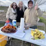 Hunger Booth Sharing Fruit: In many countries around the world fruit is a snack people can grab as they walk along a path, helping to alleviate hunger. Here in this photo Michelle Grebel, Roxanne Rogers (representing the Congregational Church) and Joe DeMasi share hunger facts and a snack of fruit along the walk).