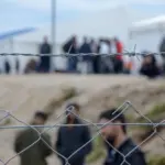 Barbed wire in refugee camp. Migrants behind chain link fence in camp. Group of people behind fence. Concept of prison^ freedom^ barrier^ security and migration. Refugees on their way to EU.