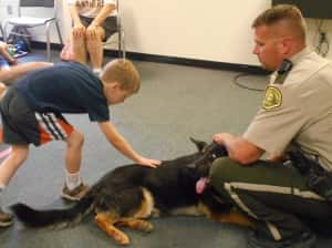 K9 Leo (middle) being petted by a kid (left) with Chief Deputy Williams (right)