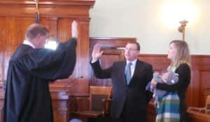 District Court Judge William Ostlund (left) swearing in County Attorney Thomas Laehn (middle) as his wife Susan and daughter Sophia (right) look on