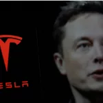 Tesla logo is displayed on smartphone screen With CEO Elon Musk in a background