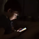 Kid who plays games on the internet at night. Portrait of a teenager boy using mobile phone on dark room