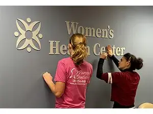 2femalestudentswithinstallingwomenshealthcentersign-jpg
