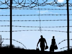 A man and woman in silhouette heading through broken border fence on the southern border of the USA.