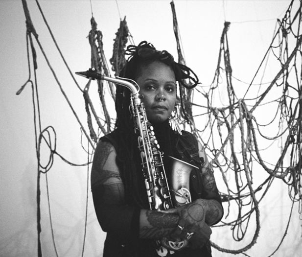 Woman holding saxophone in front of artwork