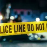 Yellow Tape Showing Text "Police Line Do Not Cross" Restricting a Crime Scene Area At Night. Close Up Aesthetic Shot with Bokeh Effect and Flickering Lights. Criminal on the Loose Strikes Again