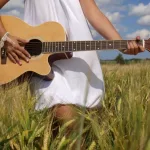 girl playing guitar in field over blue sky.