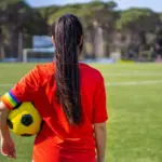 Female soccer player wearing a captain armband with the LGBT pride flag on the field. Campaign against homophobia in football. LGBTQ people in sport concept. Women's Football. Gay pride day and month.