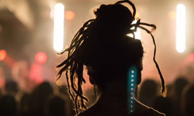 Close up portrait of an anonymous performer/ silhouette with dreadlocks^ back to camera^ watching a concert on stage with music^ retro light effect^ flashlight and spotlight in a festival.