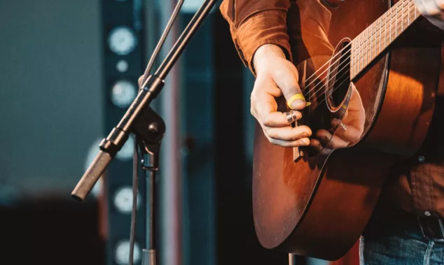 close up of hand of man playing guitar in concert on stage