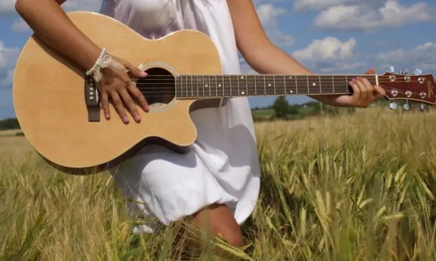 Country girl with guitar at wheat field