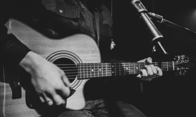 The guitarist plays an acoustic guitar with a capo in front of a microphone. The concept of music recording^ rehearsal or live performance.
