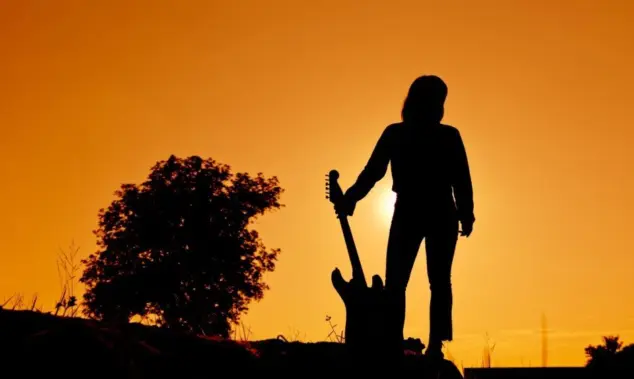 Silhouette Hipster woman with guitars in the meadow.