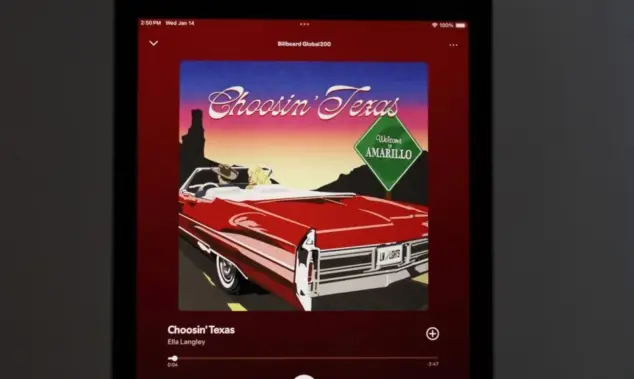 An Apple iPad displays the Spotify music streaming application^ which is playing the song "Choosin' Texas" by the artist Ella Langley