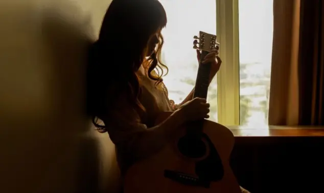 Silhouette of a young woman playing guitar alone in the dark
