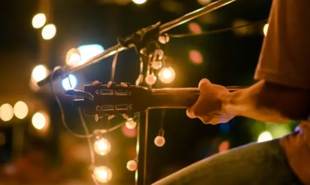 Rear view of the man sitting play acoustic guitar on the outdoor concert with a microphone stand in the front^ musical concept.
