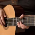 female musician playing guitar^ focus on hands/strings