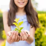 hispanic-girl-protecting-small-plant-on-earth-day-in-garden-2