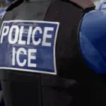 ICE police agent - Officer of Immigration and Customs Enforcement. Close-up of POLICE ICE marking on the back of a stab proof vest uniform worn by a trio of police officers at the scene of an incident