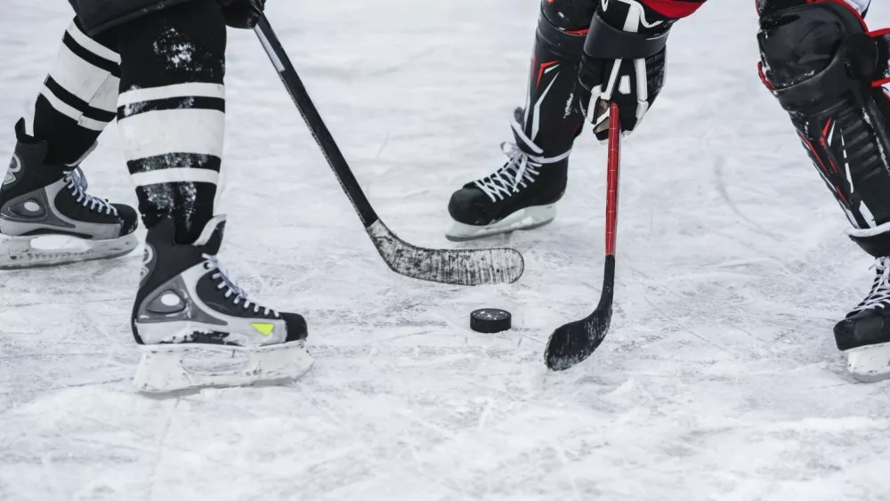 close-up of hockey puck, sticks, two players on ice during the game