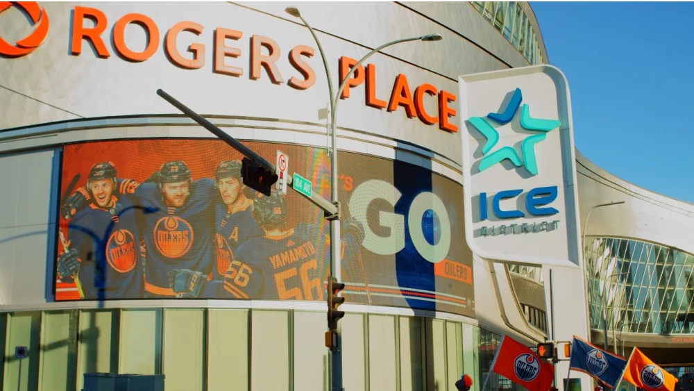 Edmonton Oilers hockey team fans waving flags outside Rogers Place stadium, with Oilers hockey players pictured on the LED billboard. Edmonton, Alberta, Canada