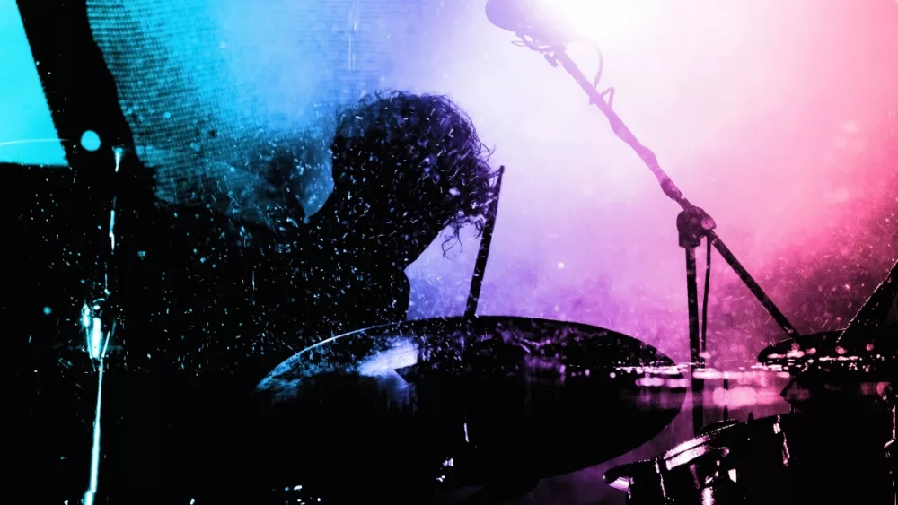 Silhouette of a drummer playing under vibrant pink and blue stage lights, capturing the energy and motion of a live music performance.