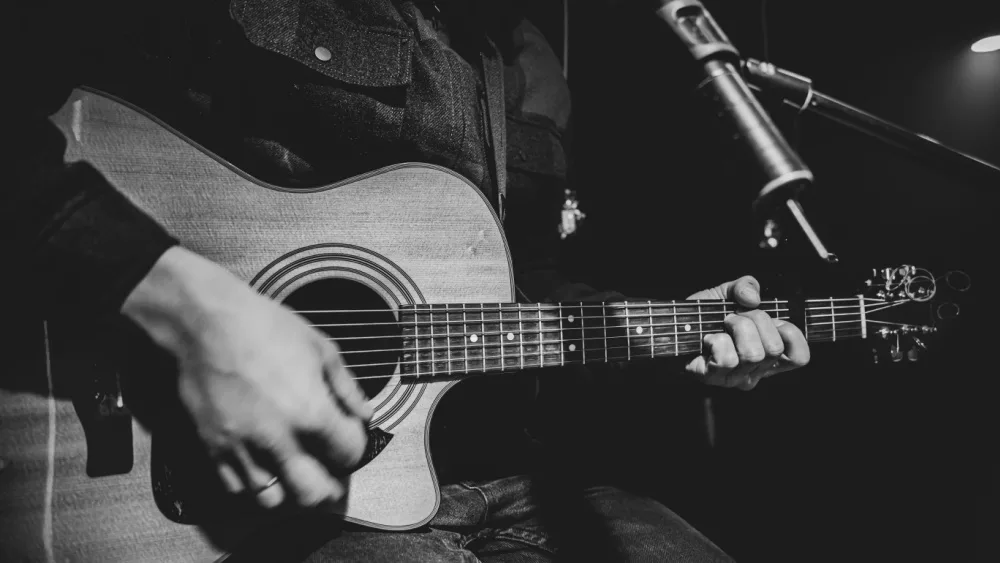 The guitarist plays an acoustic guitar with a capo in front of a microphone. The concept of music recording, rehearsal or live performance.