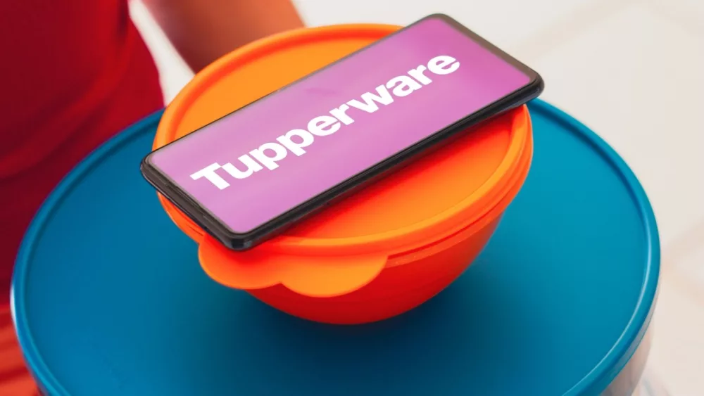 In this photo illustration, a person carries various plastic products (containers) and a smartphone shows the Tupperware logo