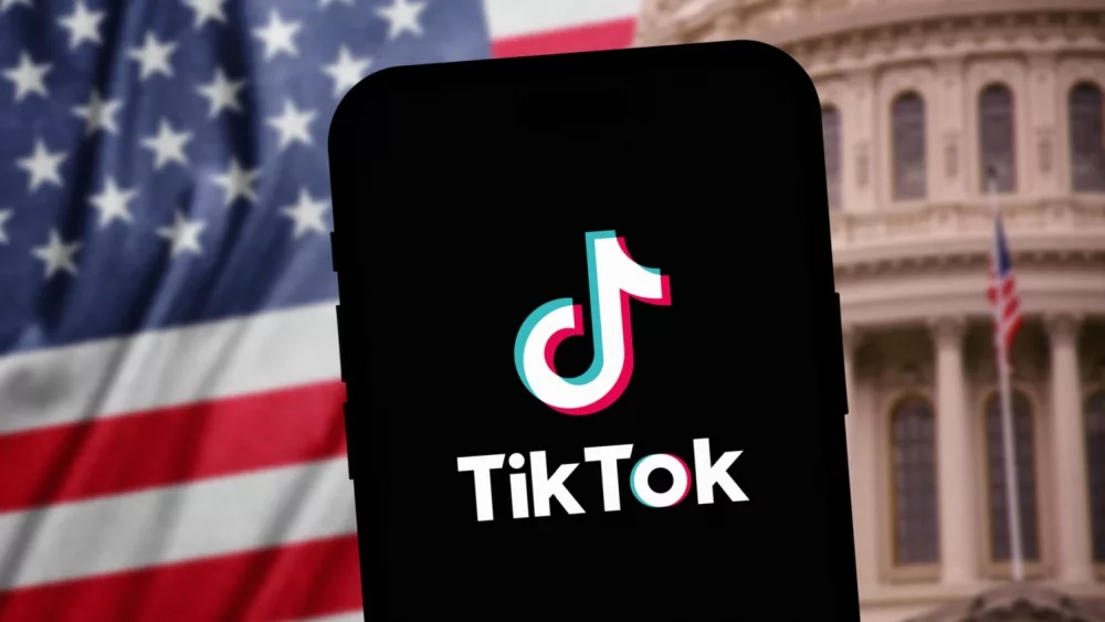 TikTok Logo on phone - sharp in the foreground, while American Congress building and US flag is blurred in the background, Concept of TikTok ban in US.