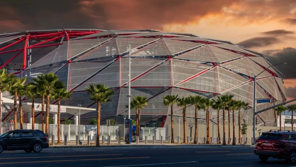 The Intuit Dome with cars driving on the street, lush green palm trees and powerful clouds at sunset in Inglewood California USA. Inglewood, California USA - 10 22 2024