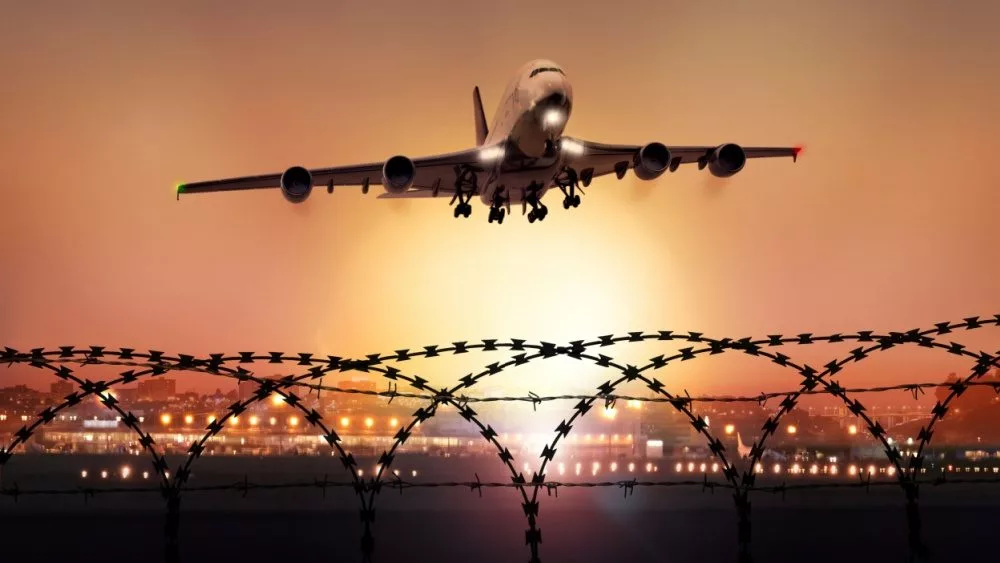 Passenger plane takes off at dusk, in the background the lights of the airport can be seen and in the foreground a barbed wire fence