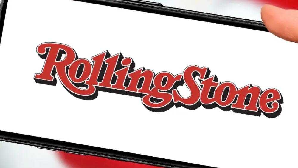 Rolling Stone magazine logo on smartphone screen against the background of the USA flag . Close-up hands holding smartphone .Company capitalization