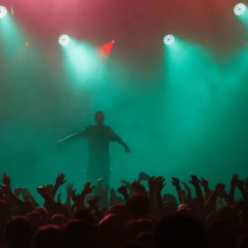 Rap singer performing on concert in music hall. Silhouette of rapper singing on stage in night club. Popuar hip hop music festival. Crowd of fans partying on dance floor