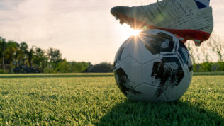 athlete-standing-with-ball-on-football-field-during-sunrise-soc