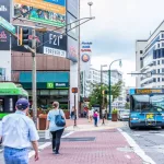 Downtown area of city in Maryland with cars on street^ bus^ and shopping mall stores^ shops and people.