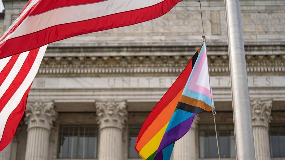 Waving Pride LGBT flag next to the flag of USA