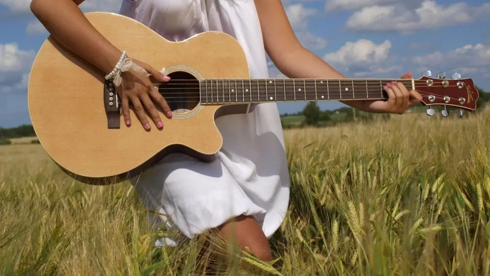 Country girl with guitar at wheat field