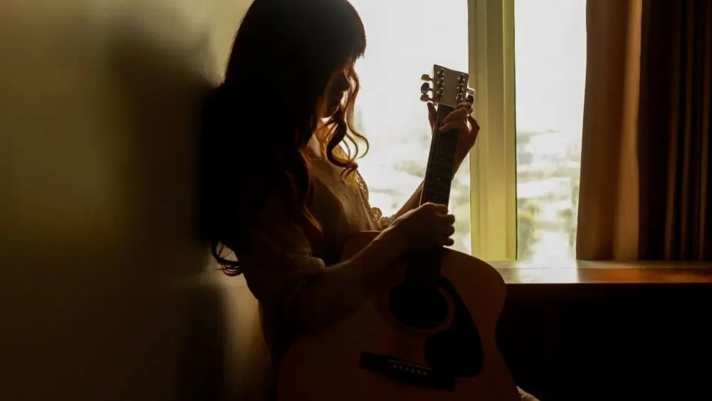 Silhouette of a young woman playing guitar alone in the dark