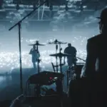 rock band viewed from behind the stage performing to sold-out audience; view of drummers^ guitarists in silhouette in hazy photo